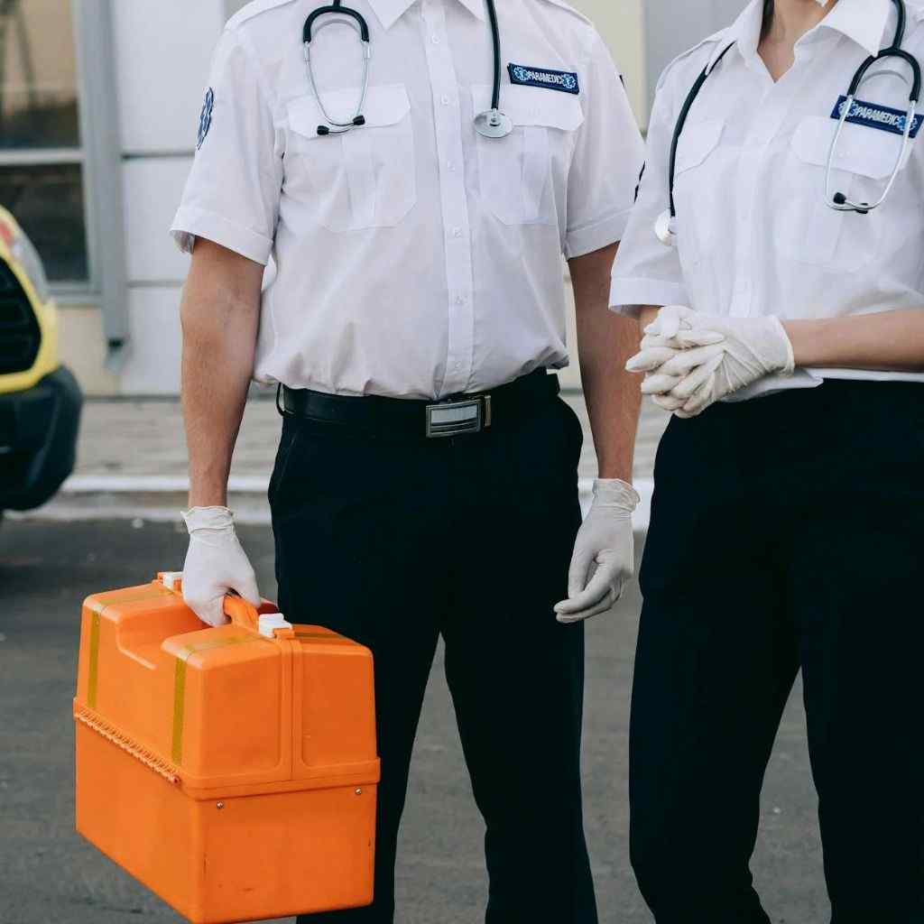 Two paramedics in uniform holding a medical kit next to an ambulance.